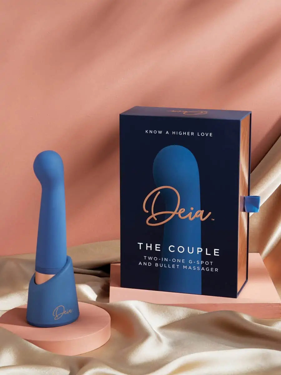 The Couple - Deia - Blue silicone dual-motor vibrator with ergonomic curves next to navy Deia packaging on peach fabric, ouiboutique. - 2 moteurs ou +, anal, clitoridien, point g, prostate, vibrateur